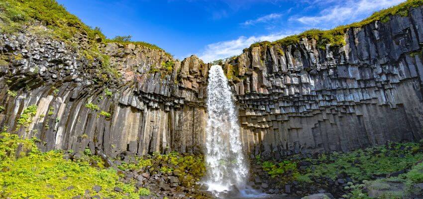 Schmaler Wasserfall umgeben von einer Steinmauer.