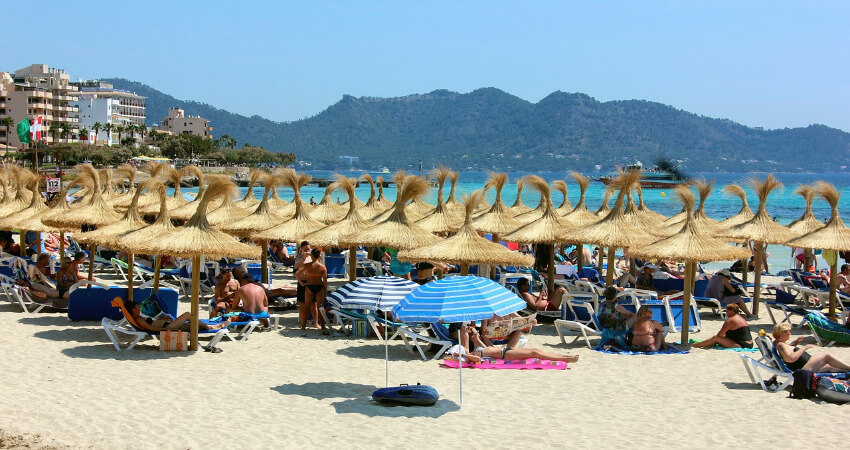 Viele Touristen am Sandstrand unter Stroh Sonnenschirme.