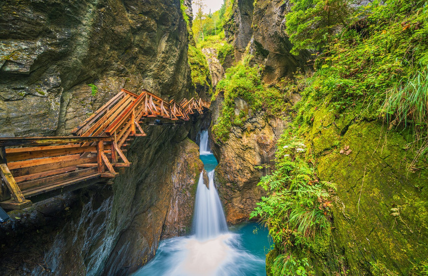 Eine schmale Schlucht mit zwei Wasserfällen und entlang der Steinwand ein Holzsteg.