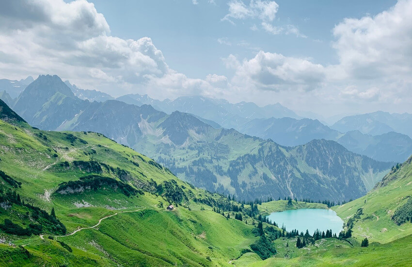 Berge grün bewachsen mit Gras und Bäumen. Mittendrin ein kleiner Bergsee.