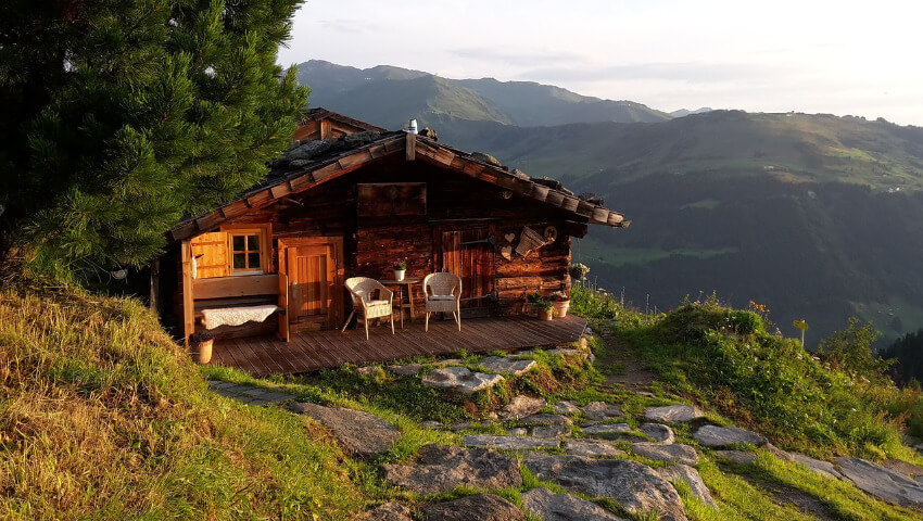 Eine kleine Berghütte aus Holz mit einer Terrasse vorm Eingang.